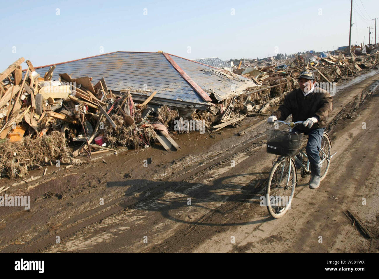 Un uomo giapponese cavalca la sua bicicletta passato i detriti dello tsunami la devastazione causata dal 9,0-terremoto di magnitudine di Sendai, Giappone, 13 marzo 2011. Foto Stock