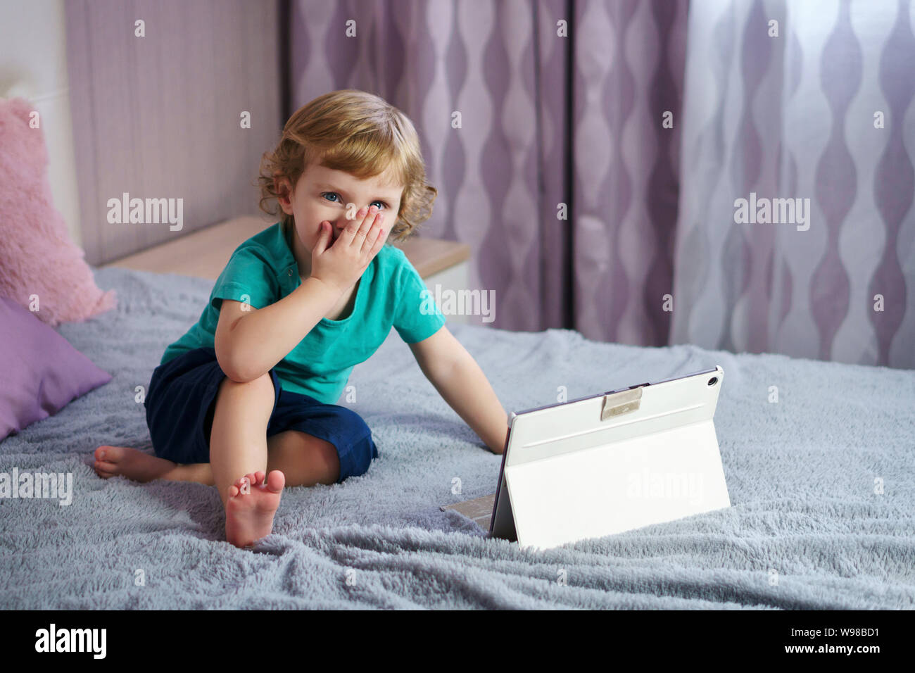 Golden-pelose, affascinanti orologi bambino vignette su un computer tablet  mentre è seduto su un letto in camera con i genitori. Passatempo  interessante da soli Foto stock - Alamy