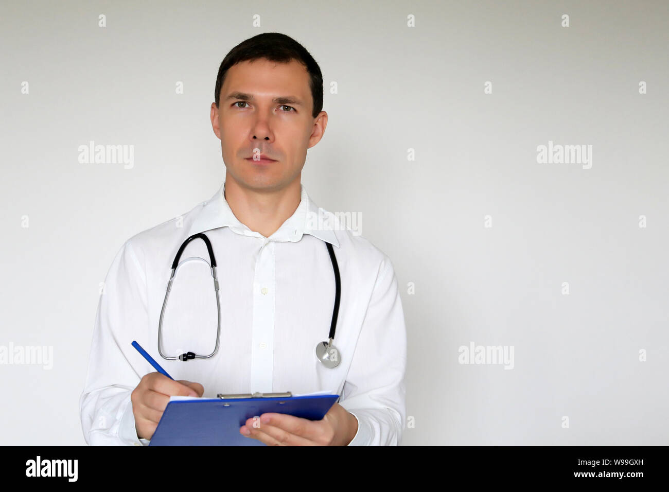 Medico con stetoscopio scrive una prescrizione in piedi su sfondo bianco. Ritratto di un medico di sesso maschile, il concetto di medicina, terapeuta, esame Foto Stock