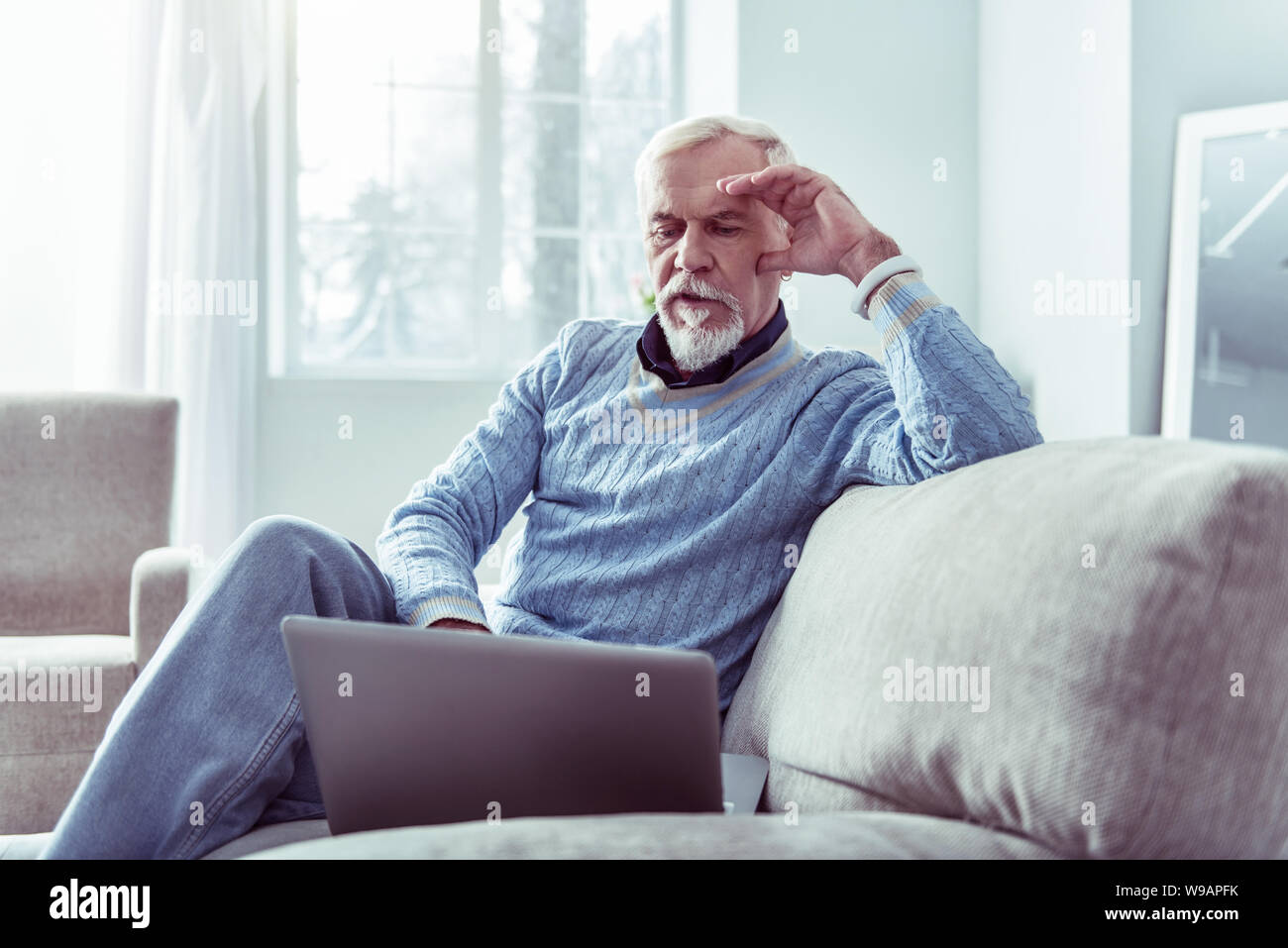 Ritirato moderno uomo bianco che indossa smart watch guardando al suo computer portatile Foto Stock