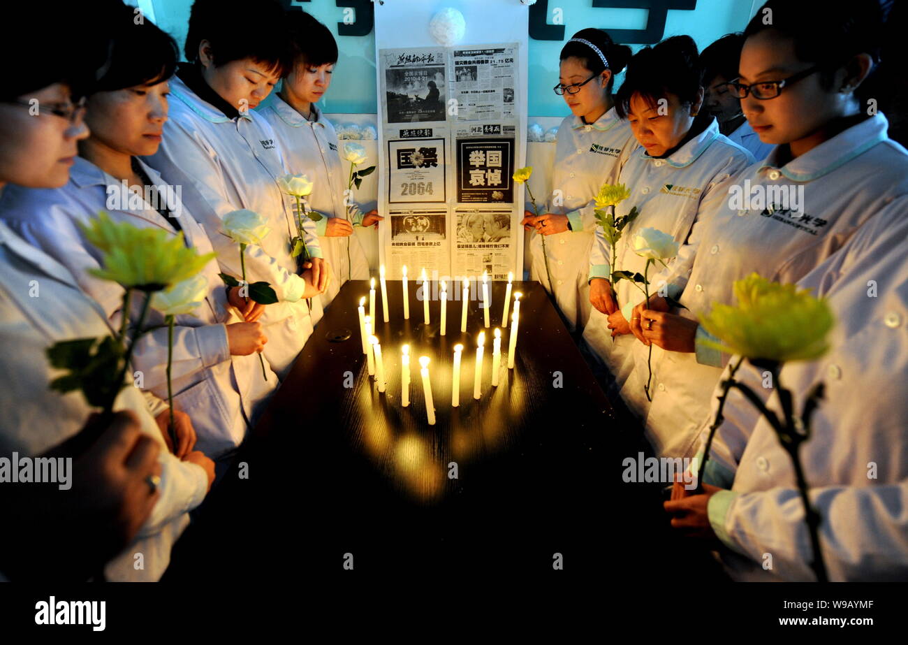 Lavoratori cinesi holding fiori osservare tre minuti di silenzio al cordoglio per le vittime del 7,1-terremoto di magnitudine in Yushu county di Northwest Chi Foto Stock