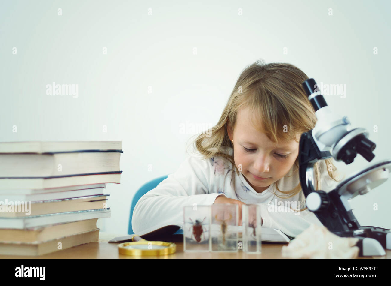 Bambina giocando scienziato tra pile di libri con un microscopio Foto Stock