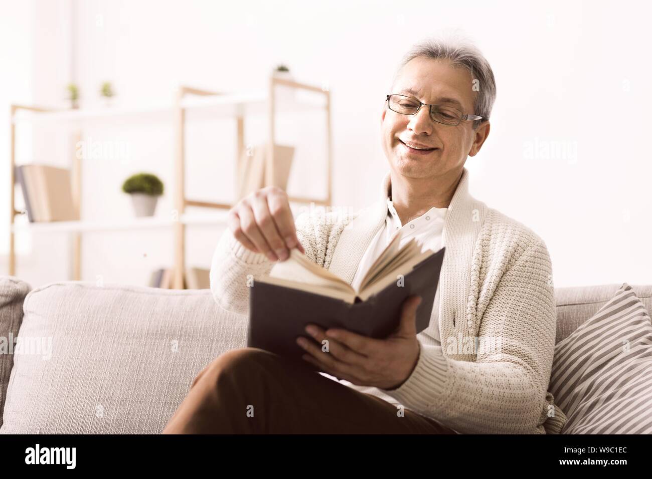 Senior uomo in bicchieri gustando un buon libro con sorriso Foto Stock