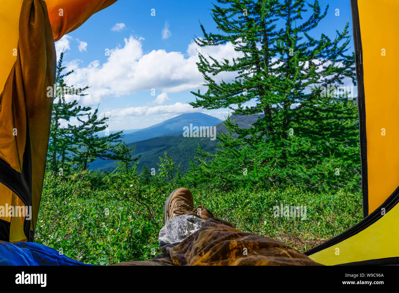 Una mattina di sole in una escursione in montagna - una vista da un turista tenda; le gambe di un escursionista giacenti in esso in scarponi da montagna, sono visibili Foto Stock