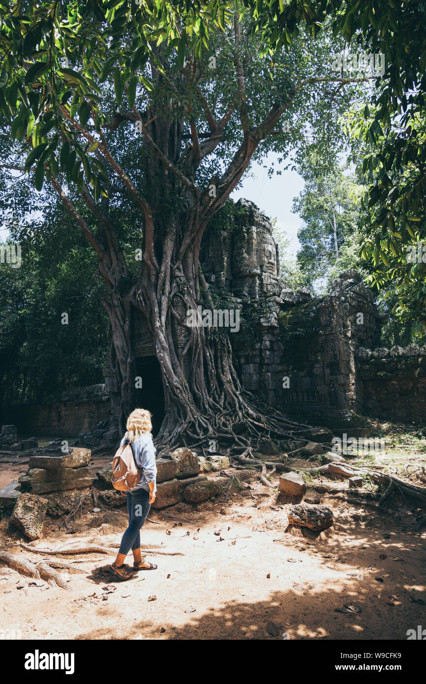 Caucasian donna bionda scoprendo le rovine di Angkor Wat tempio complesso in Siem Reap, Cambogia. Albero che cresce sul tetto del tempio cancello di ingresso arc Foto Stock