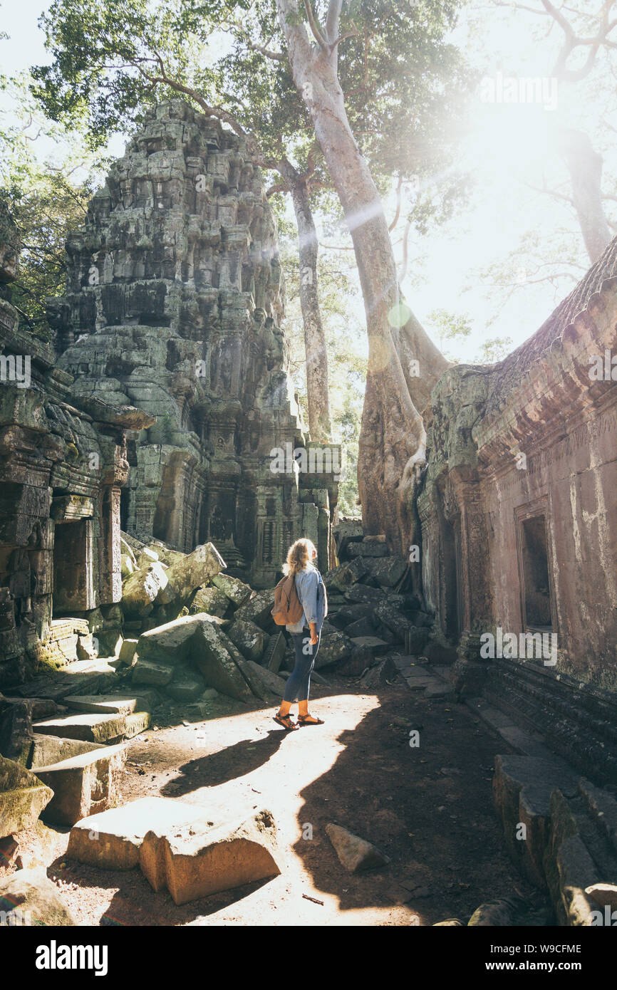 Caucasian donna bionda scoprendo le rovine di Angkor Wat tempio complesso in Siem Reap, Cambogia. Albero che cresce sul tetto del tempio. Foto Stock