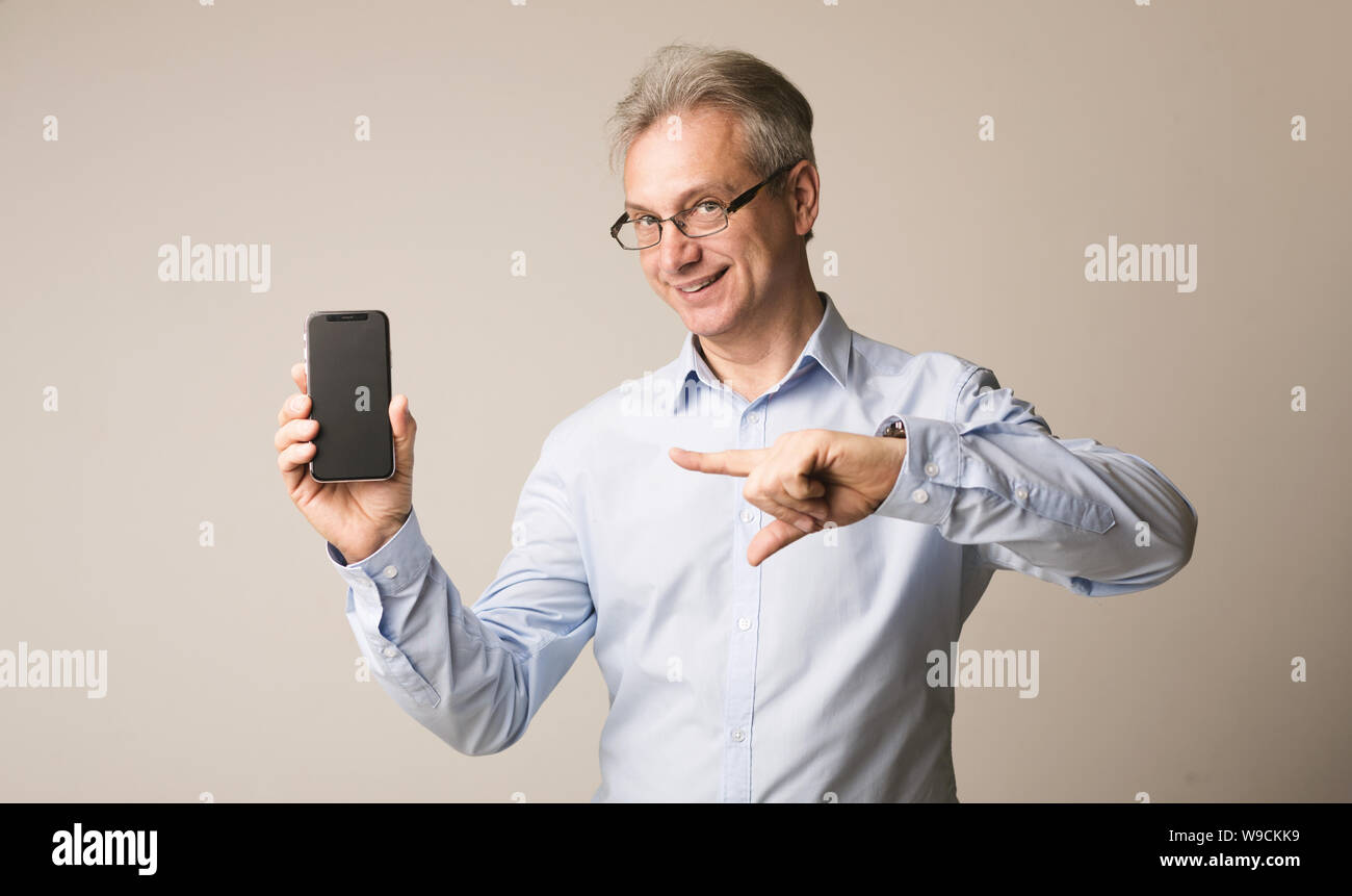 Senior uomo presentando smartphone e puntando su di esso Foto Stock