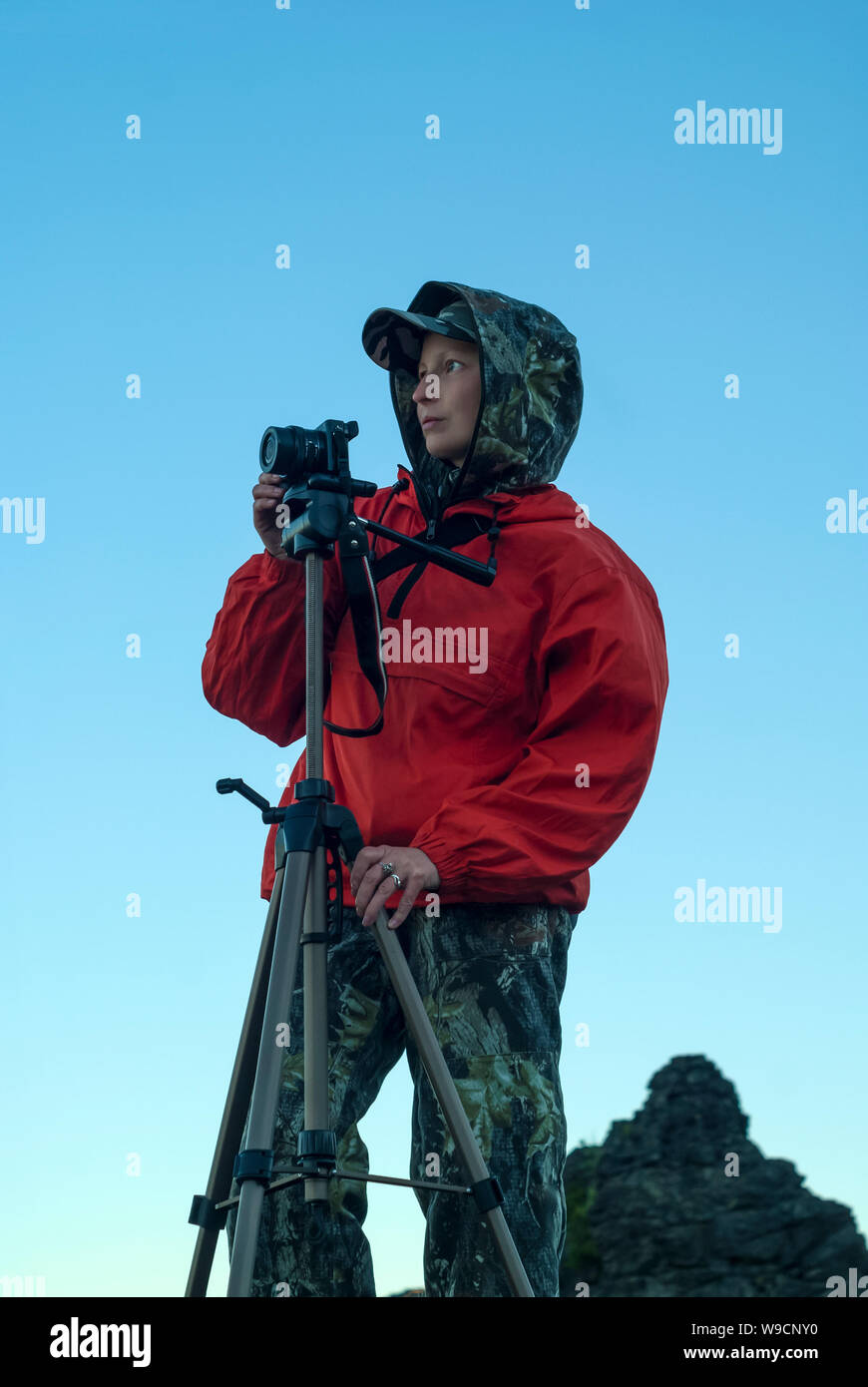 La ragazza di escursionismo vestiti guarda nella distanza, preparazione per scattare una foto della fotocamera su un treppiede Foto Stock
