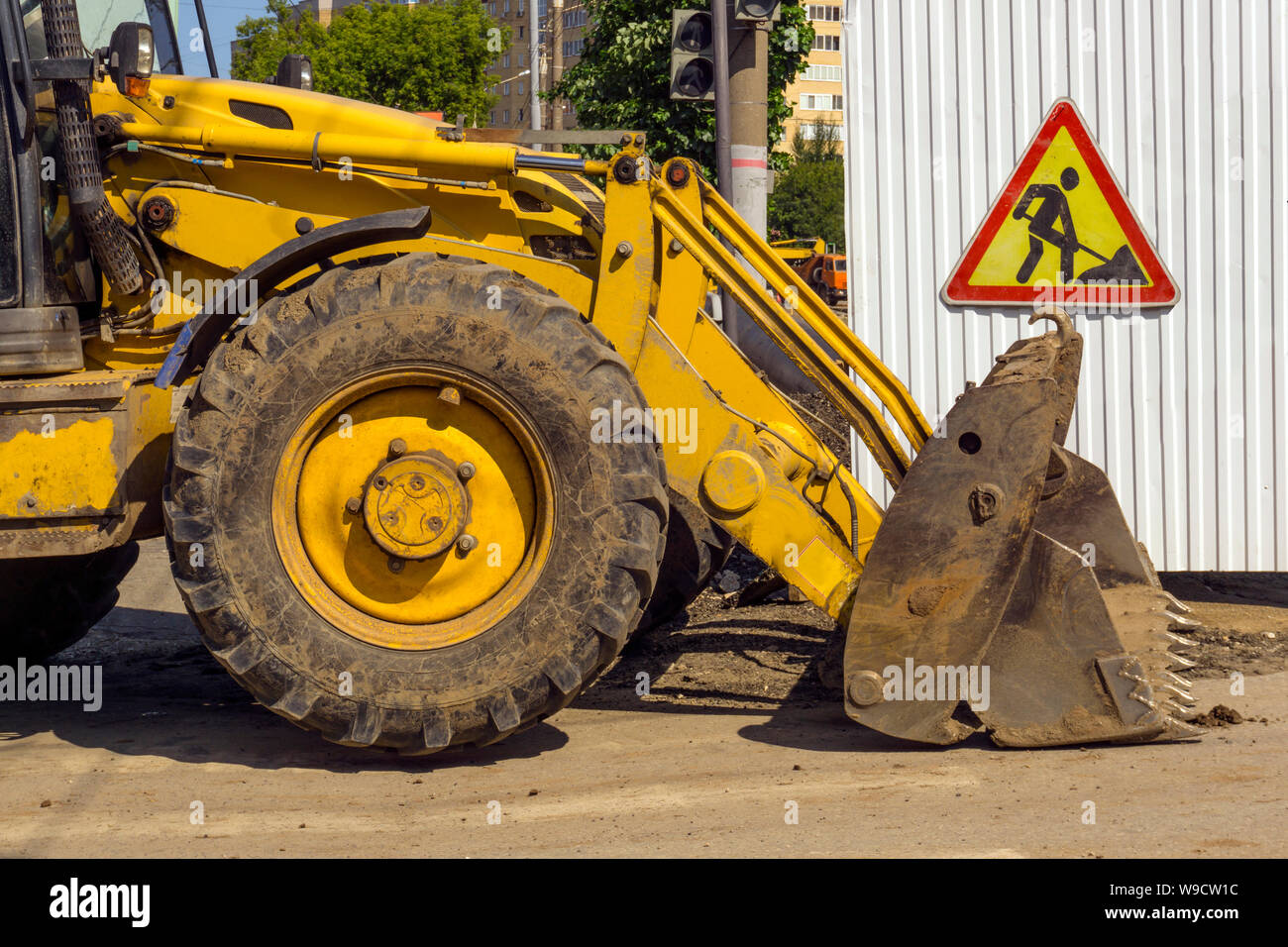 Cava di sporco permanente del caricatore attraverso la strada riparato accanto al segno "opere stradali' appeso alla recinzione temporanea Foto Stock