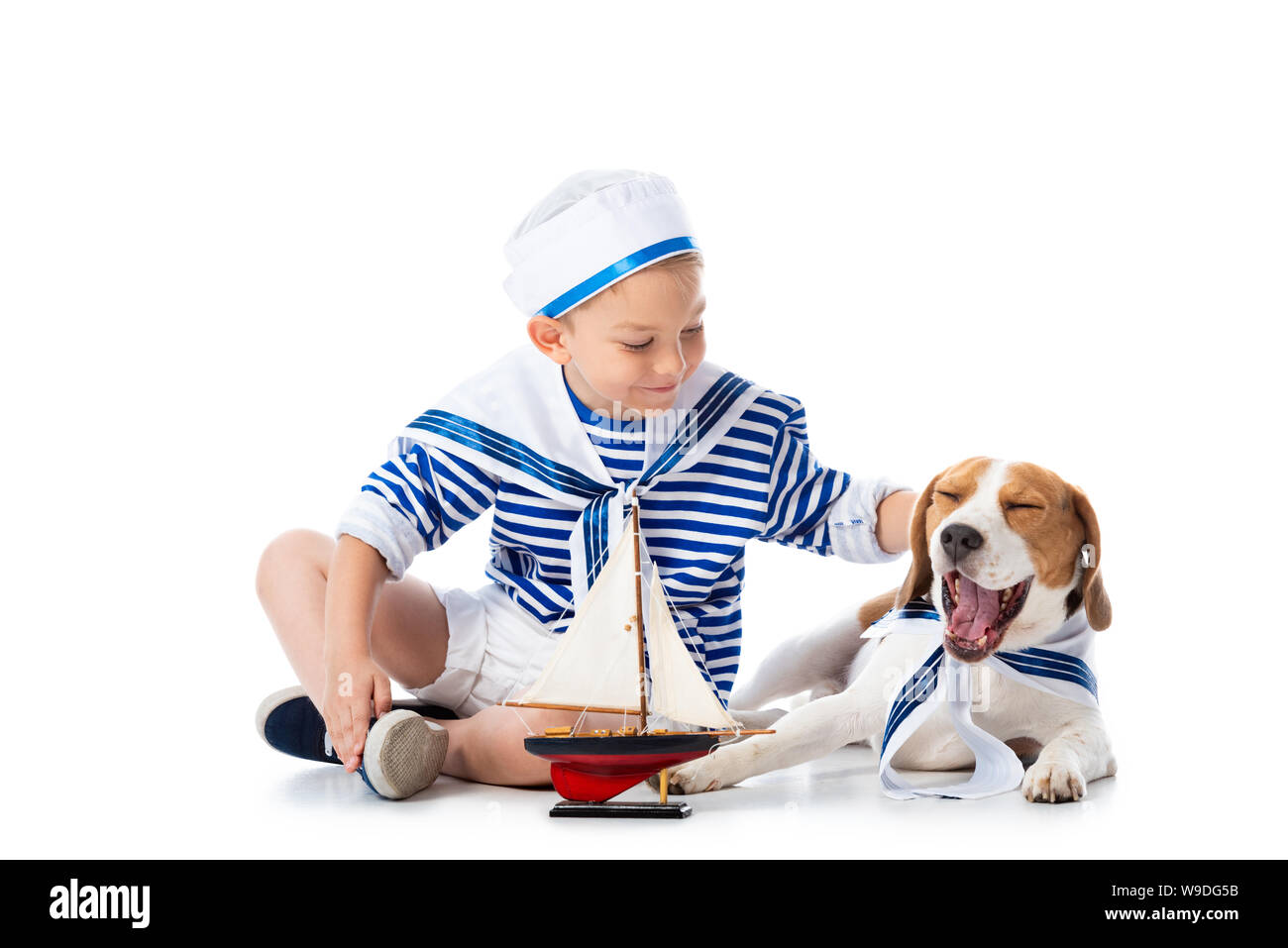 Preschooler bambino in sailor suit con nave giocattolo e cane beagle su bianco Foto Stock