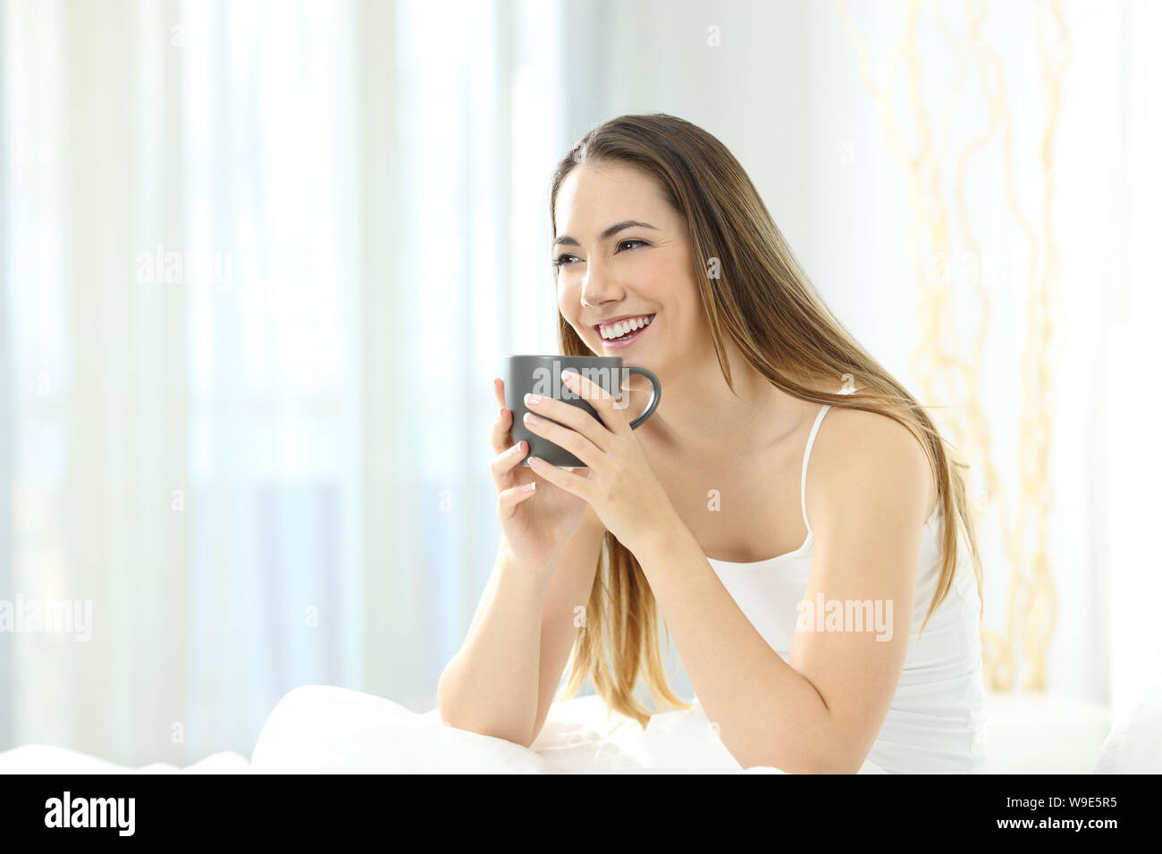 Donna felice beve caffè sul letto la mattina a casa o camera di albergo Foto Stock