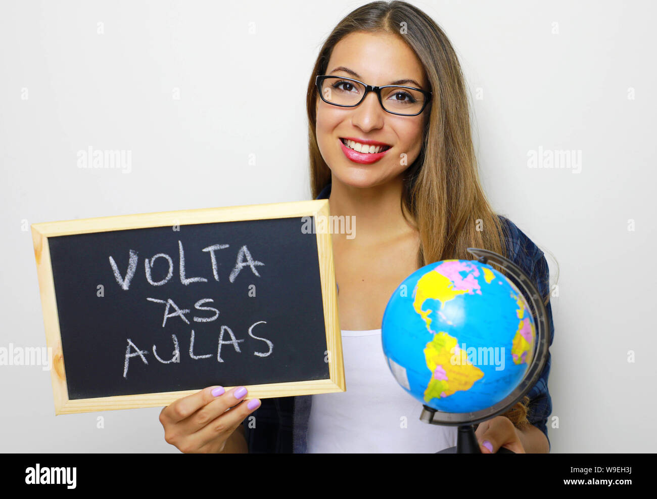 Brasiliano femmina giovane insegnante holding globe e blackboard portoghese con la scritta 'Volta come aule' (torna a scuola). Foto Stock
