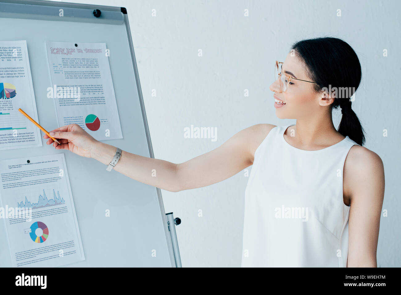 Piuttosto imprenditrice rivolto con la matita sul foglio per lavagna a fogli mobili con infographics Foto Stock