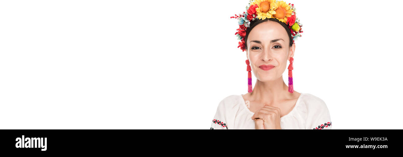 Felice bruna giovane donna in nazionale ucraino camicia ricamata e ghirlanda floreale isolato su bianco, scatto panoramico Foto Stock