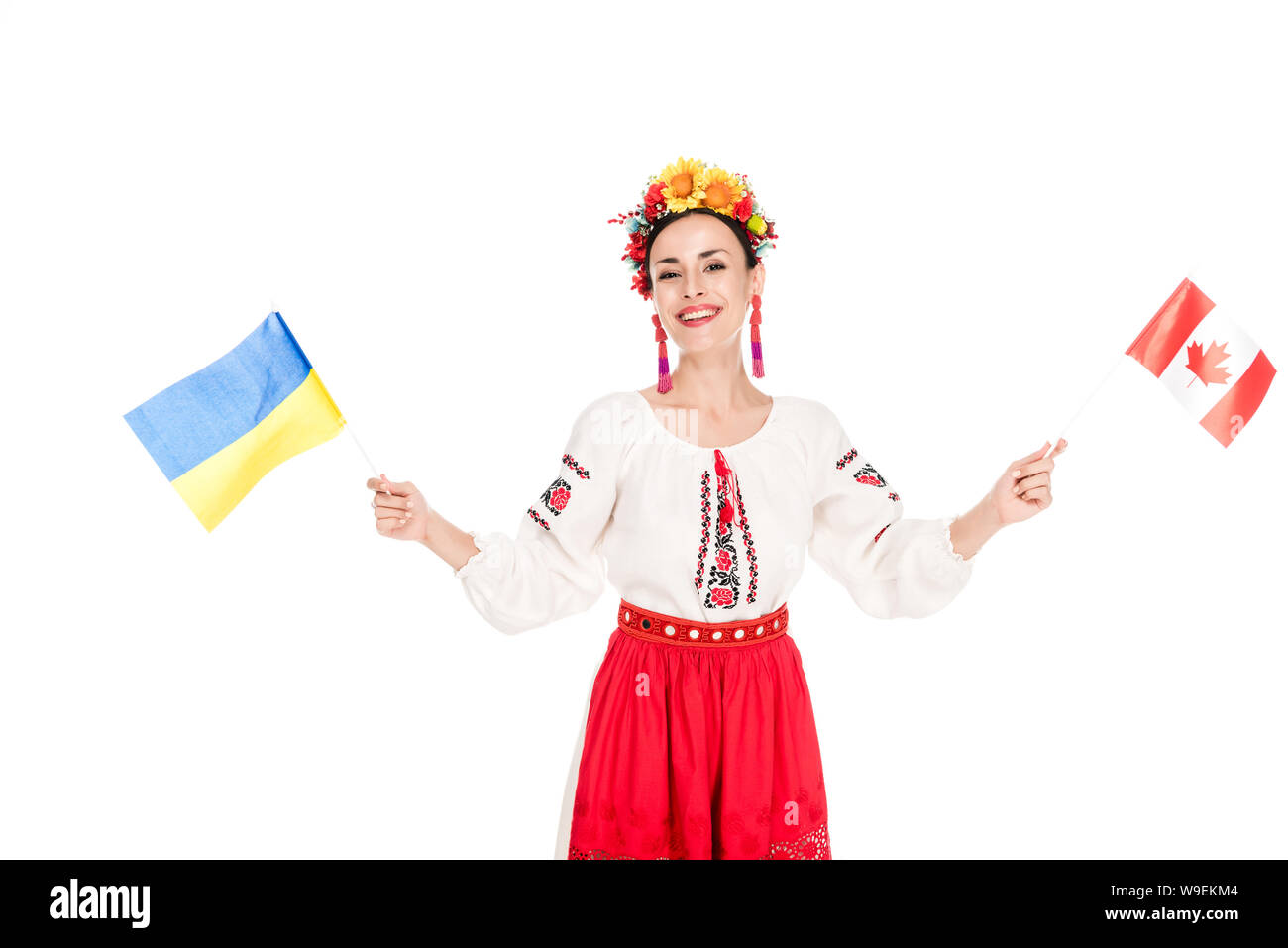 Sorridente bruna giovane donna in nazionale costume ucraino tenendo le bandiere di Ucraina e Canada isolato su bianco Foto Stock