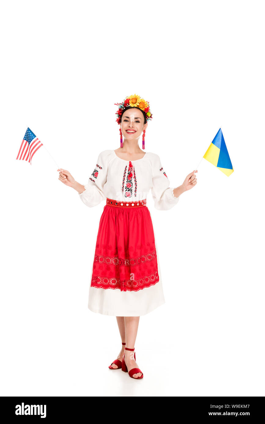 Felice bruna giovane donna in nazionale costume ucraino azienda americana e bandiere ucraine isolato su bianco Foto Stock