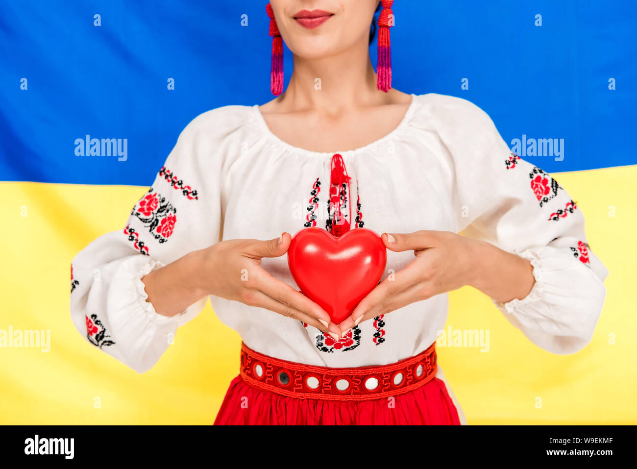 Vista parziale di giovane donna in nazionale ucraino azienda costume cuore rosso con bandiera di Ucraina sullo sfondo Foto Stock