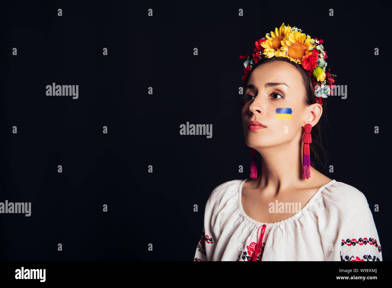 Bruna giovane donna in nazionali ucraine costume e una corona di fiori alla ricerca di distanza isolato su nero Foto Stock