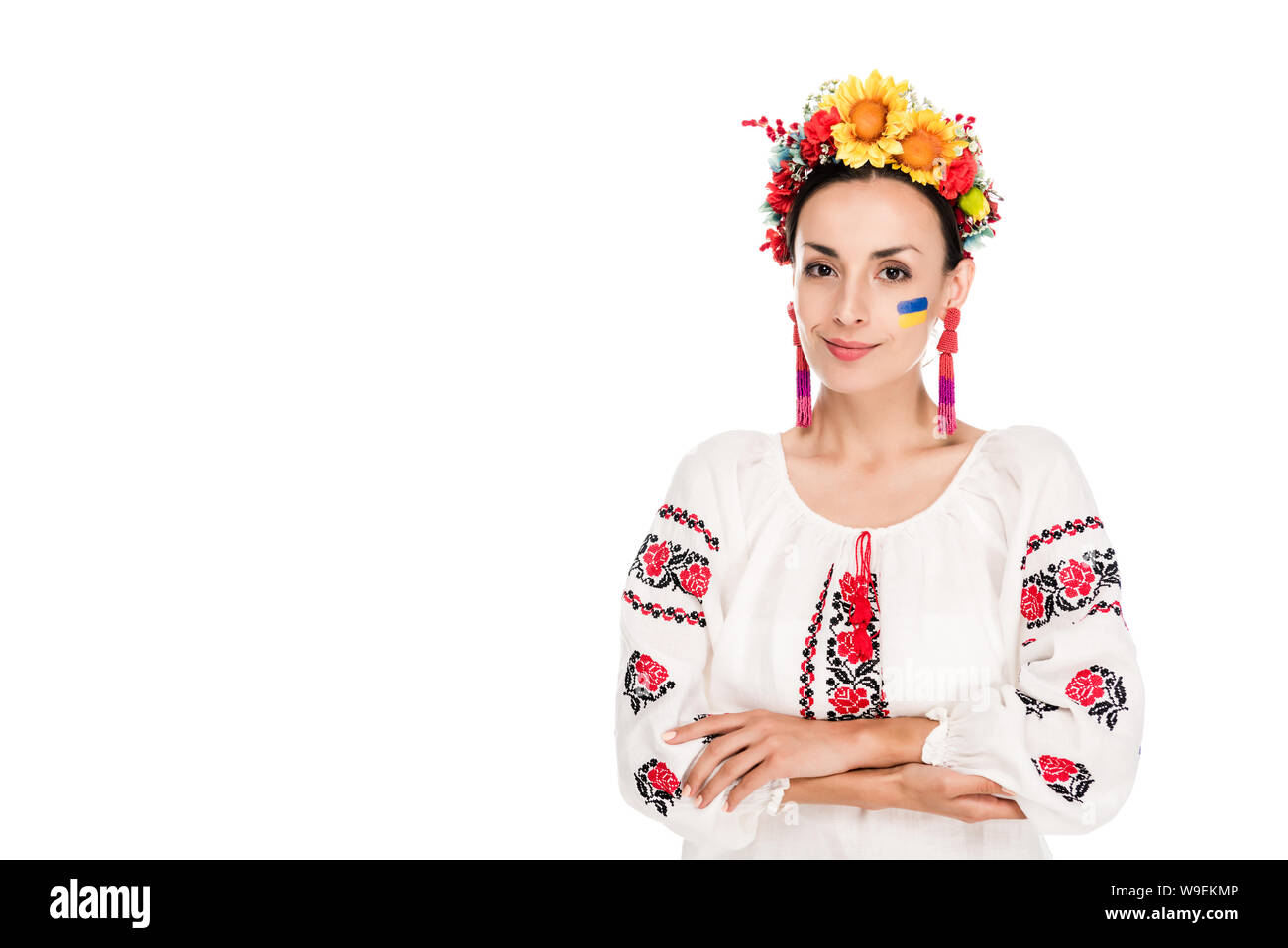 Bruna giovane donna in nazionale ucraino camicia ricamata e ghirlanda floreale con bracci incrociati isolato su bianco Foto Stock