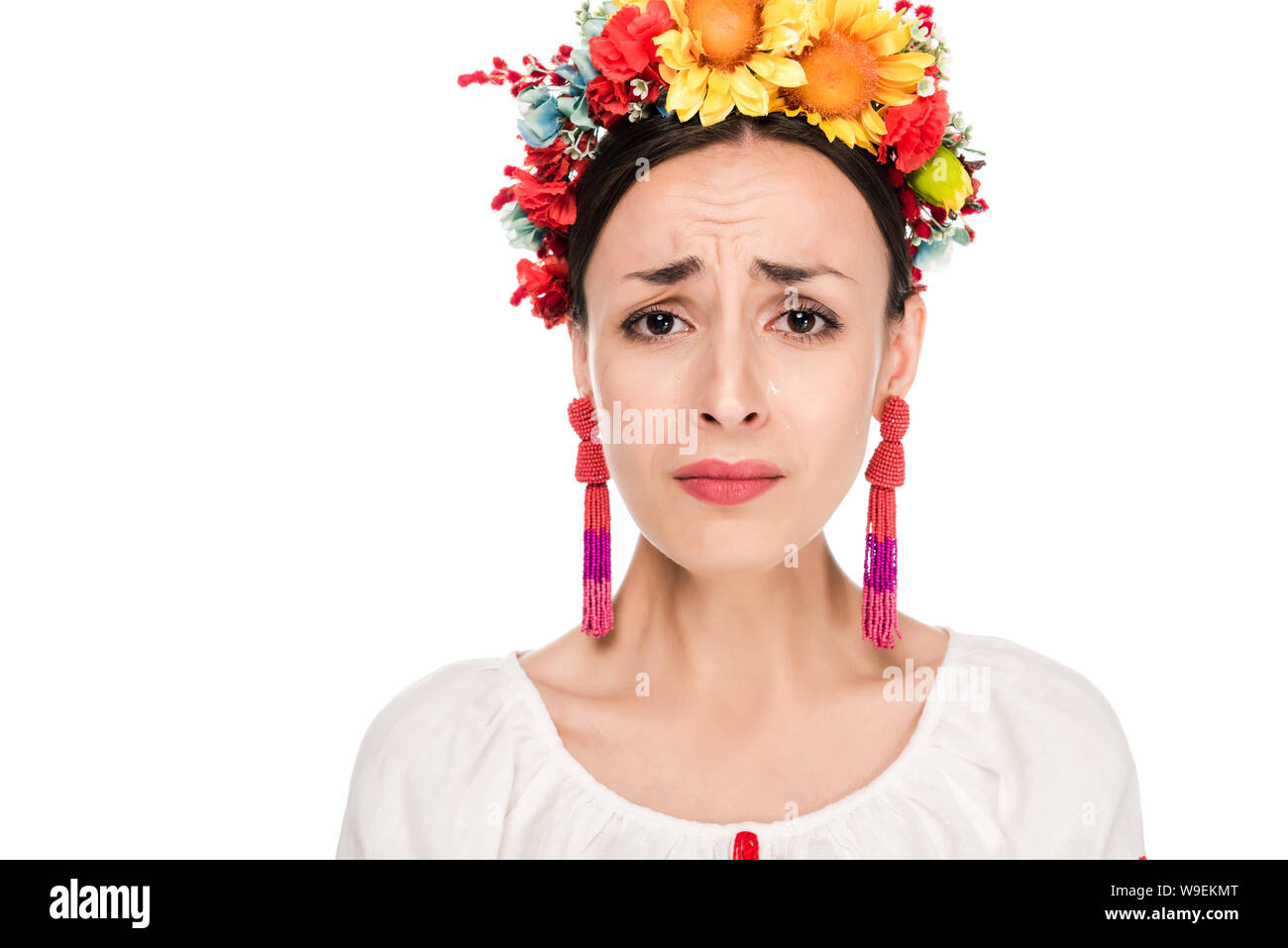 Sconvolto bruna giovane donna in nazionale ucraino camicia ricamata e ghirlanda floreale isolato su bianco Foto Stock