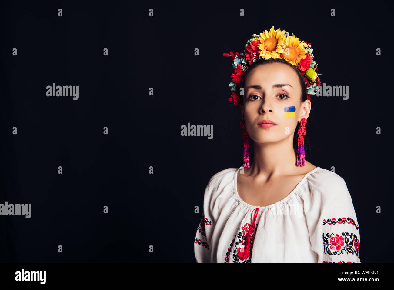 Bruna giovane donna in nazionale ucraino e costume ghirlanda floreale guardando la telecamera isolato su nero Foto Stock