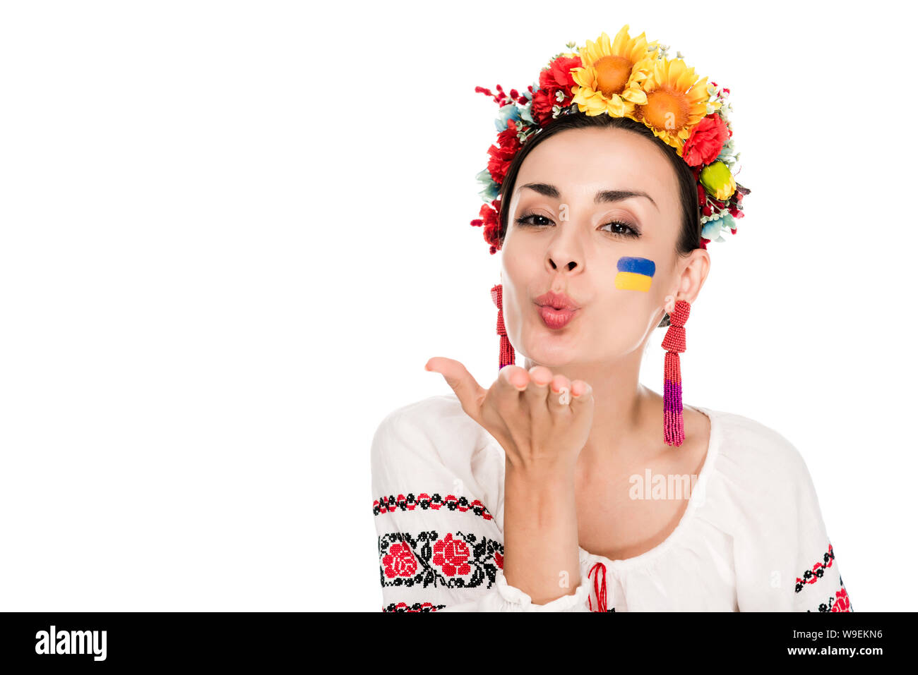 Bruna giovane donna in nazionale ucraino camicia ricamata e ghirlanda floreale soffiando kiss isolato su bianco Foto Stock
