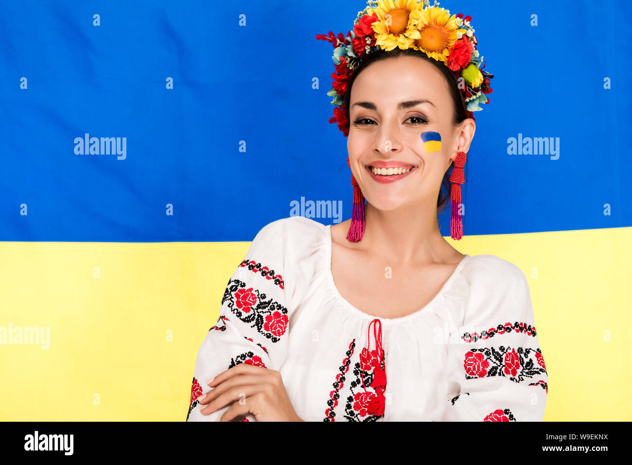 Felice bruna giovane donna in nazionale ucraino e costume ghirlanda floreale con bandiera di Ucraina sullo sfondo Foto Stock