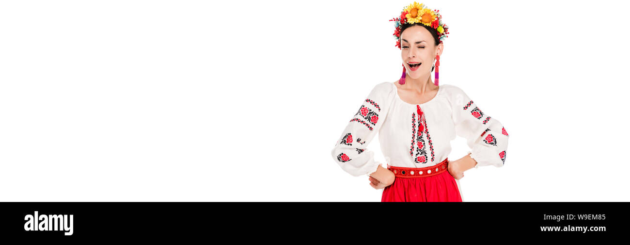 Bruna giovane donna in nazionali ucraine costume con le mani sui fianchi winking isolato su bianco, scatto panoramico Foto Stock