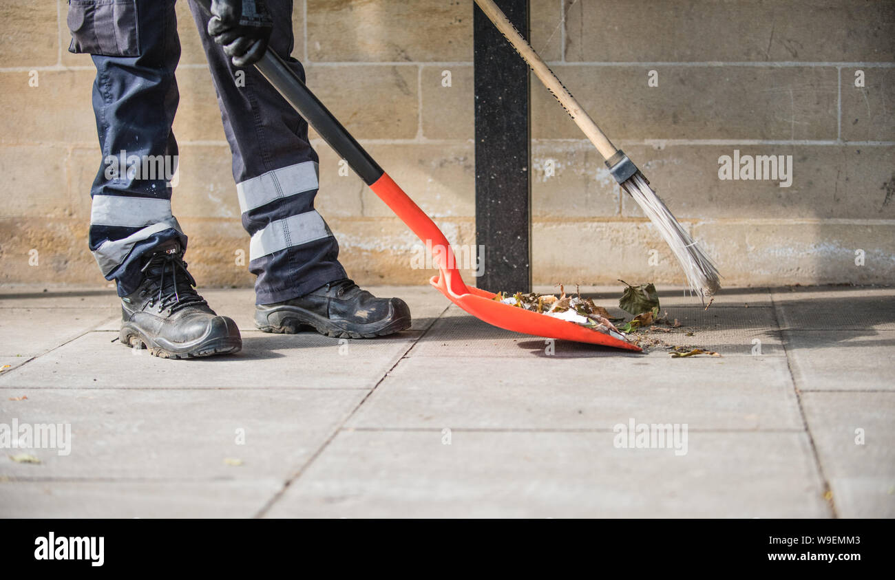 Pulizia della strada lavoratore spazia su caduto foglie su un marciapiede mantenendo la città pulita e ordinata con una pala e una spazzola e un apritoio Foto Stock