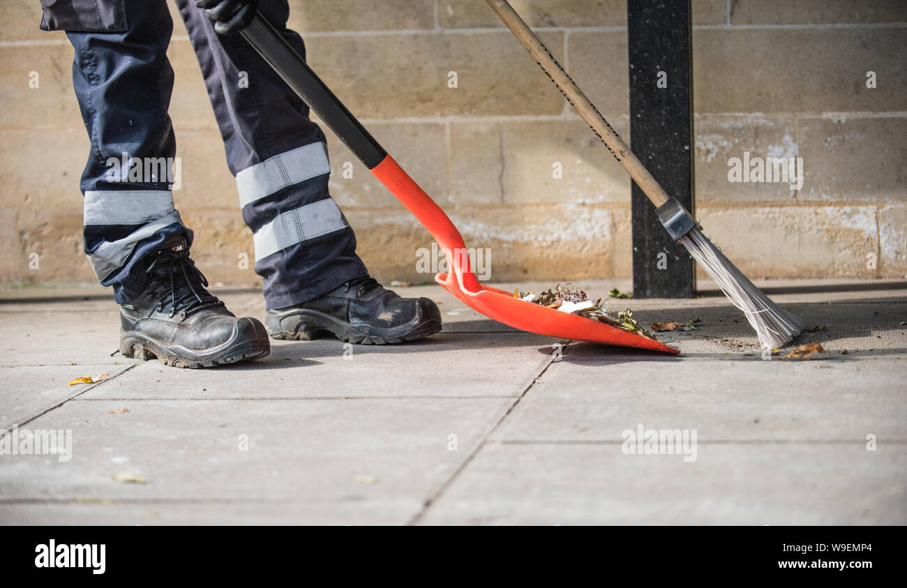 Pulizia della strada lavoratore spazia su caduto foglie su un marciapiede mantenendo la città pulita e ordinata con una pala e una spazzola e un apritoio Foto Stock