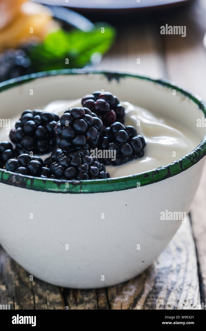 Sana colazione o brunch, preferito pasto mattutino con frutti di bosco. Yogurt freschi estate more nelle zone rurali la tazza sul tavolo di legno, close up, selettivo f Foto Stock