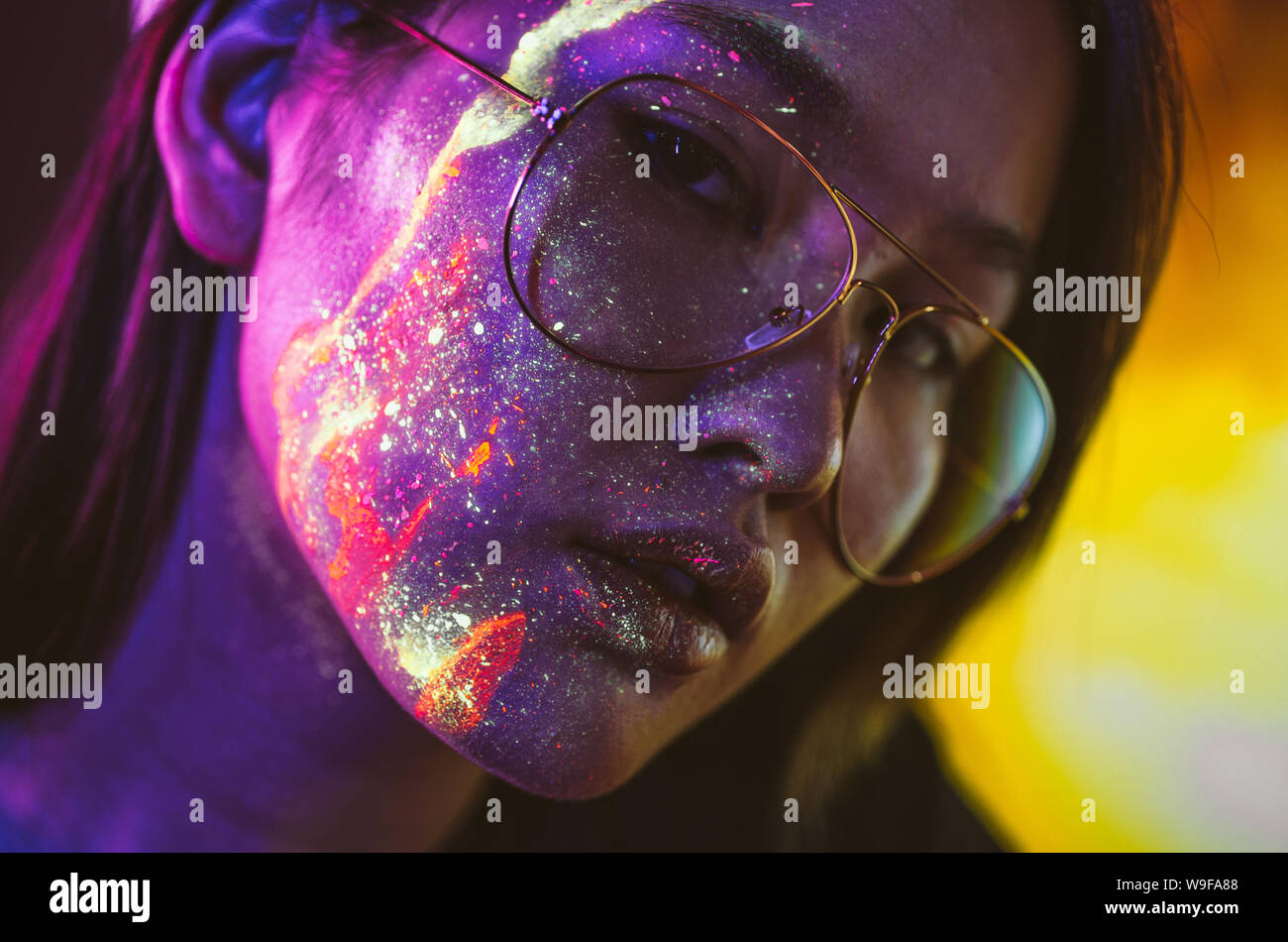 Bella giovane donna danza e facendo festa con pittura fluorescente sul suo viso. Neon ritratti del viso Foto Stock