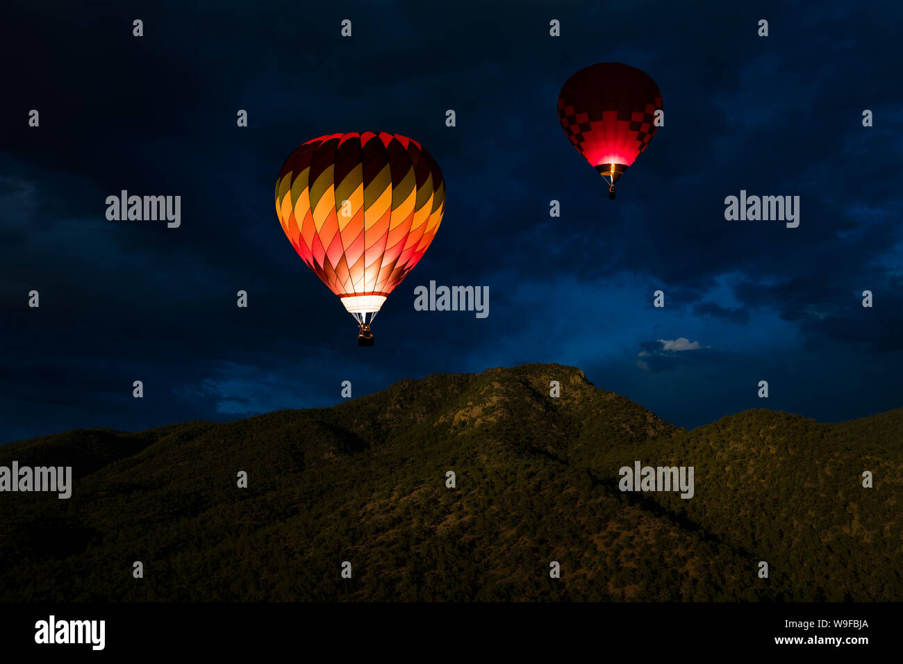 Incandescente colorate mongolfiere galleggianti in un cielo notturno su boschiva a picchi di montagna Foto Stock