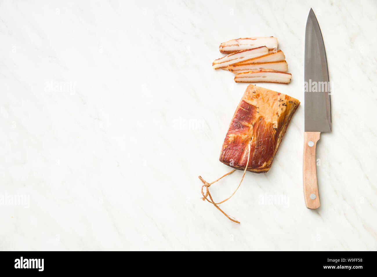 Carne affumicata. Saporita pancetta e il coltello sul tavolo bianco. Vista dall'alto. Foto Stock