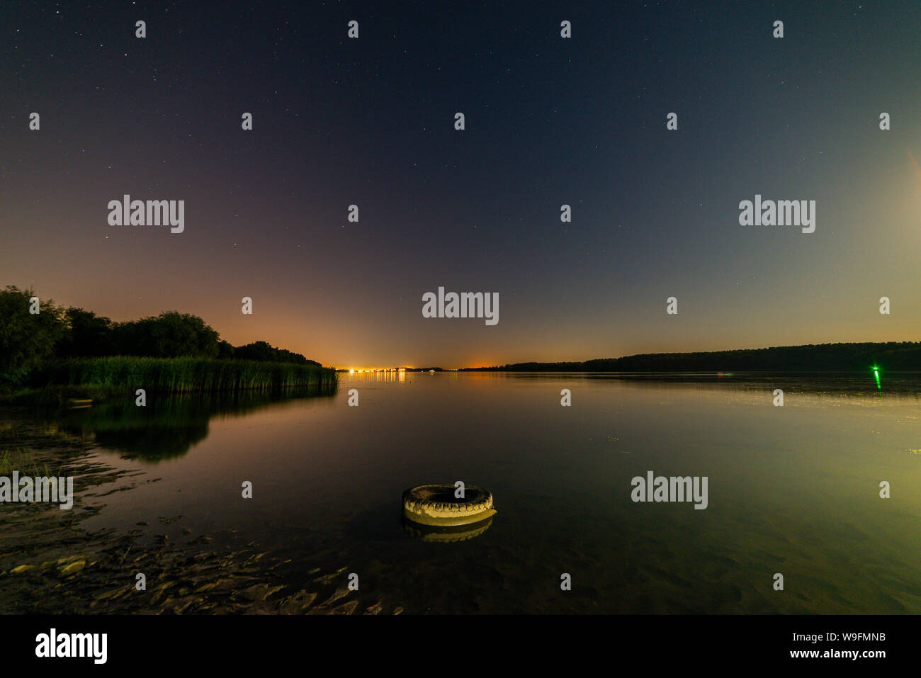 Lago o fiume riva di sabbia con alberi e blu scuro cielo stellato e luce della città sullo sfondo. Carattere tranquillo paesaggio notturno. Foto Stock