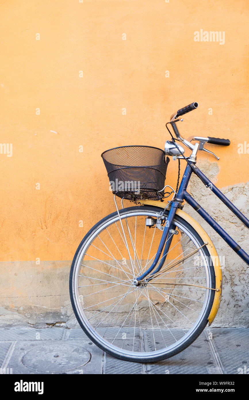 Un blu navy bicicletta con un cestello appoggiato contro una parete arancione a Pisa, Italia. Foto Stock