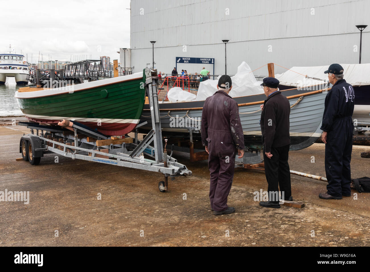 Tre uomini anziani in piedi accanto al restaurato recentemente barche di legno su una sorta di scivolo Foto Stock