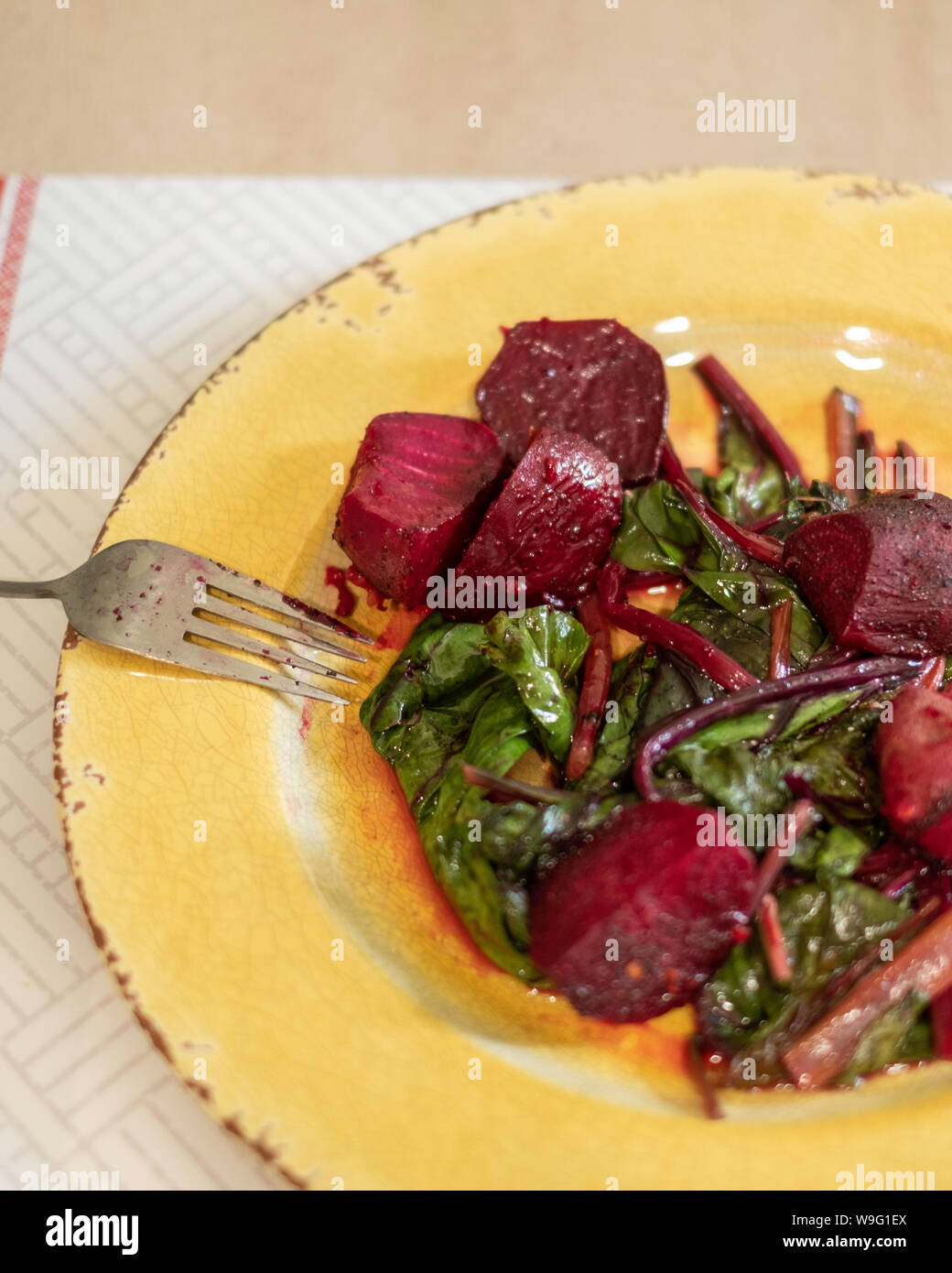 Barbabietole o barbabietole cotte calde e fresche, condite con olio d'oliva e aglio su un piatto giallo. Foto Stock