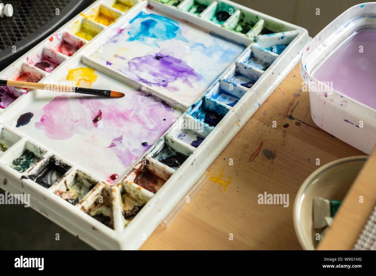 Tavolozza di un artista con spazzola ad acquerello acquerello e vernici in singoli pozzetti di vernice. Foto Stock