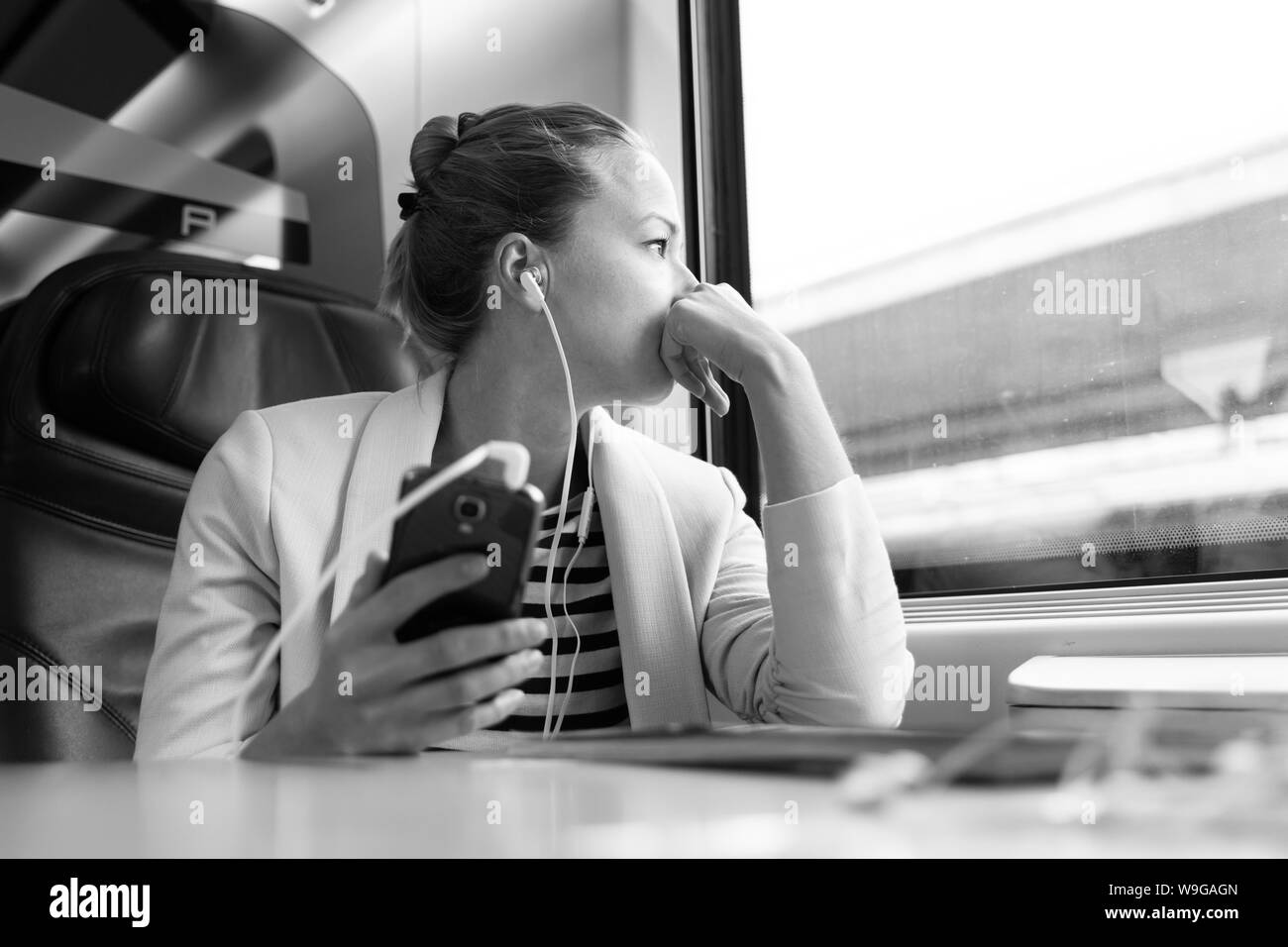 Riflessivo imprenditrice ascolto di podcast sul telefono cellulare mentre si è in viaggio in treno. Foto Stock