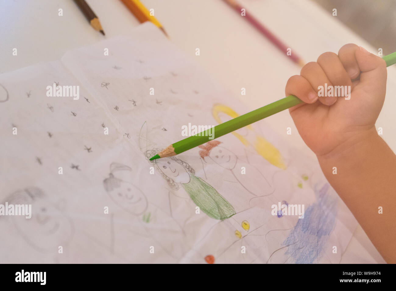 Piccola mano la colorazione di un disegno realizzato a mano con una matita verde. concetto di sviluppo di capacità artistiche nei bambini Foto Stock