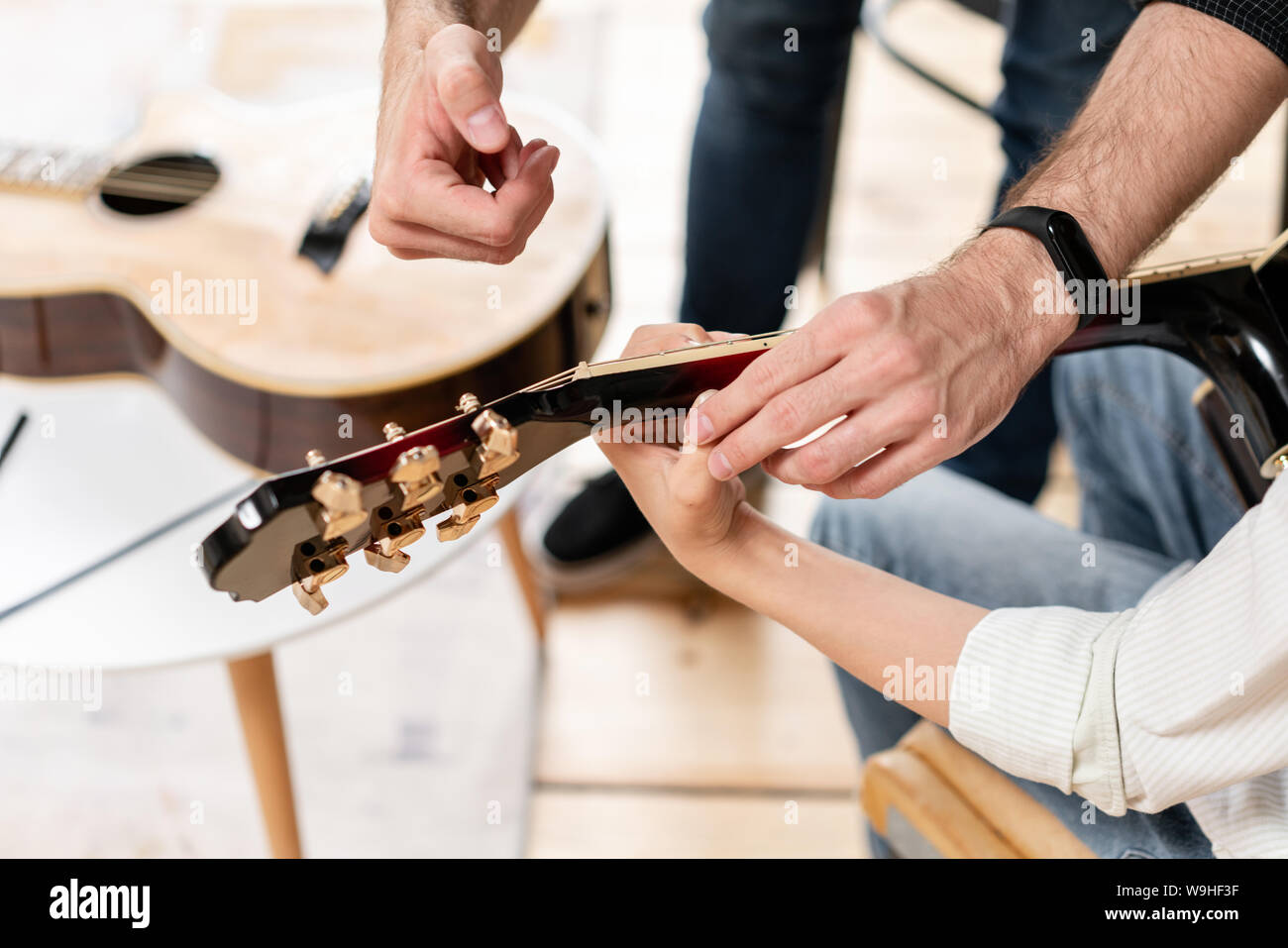 Primo piano della chitarra nelle mani del giovane ragazzo con un'altra chitarra la posa sul pavimento sullo sfondo. Foto Stock