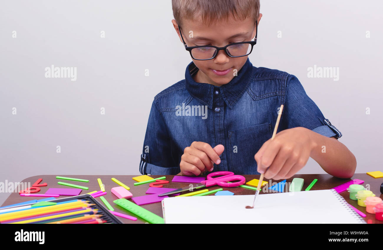 Banner ragazzo in una camicia blu e i bicchieri si siede a un tavolo su uno sfondo bianco. Attività Creative hobby disegno Foto Stock