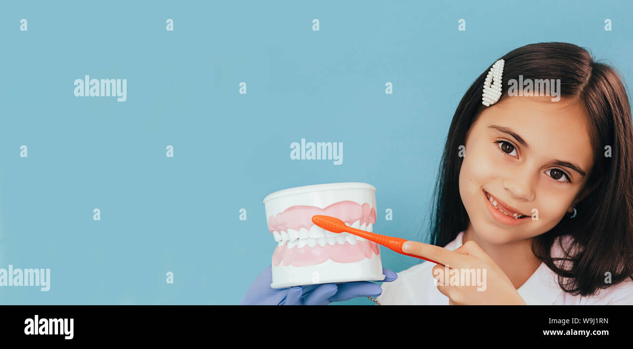 Sorridente razza mista ragazza con spazzolino da denti e denti umani modello. Il bambino mostra modo giusto la spazzolatura dei denti su sfondo blu Foto Stock