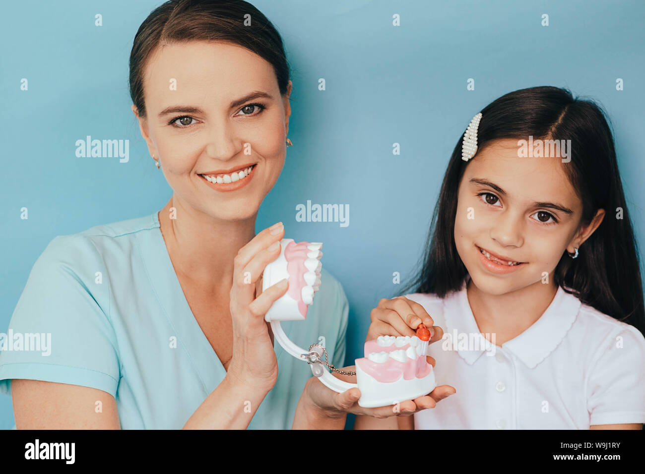 Sorridente razza mista ragazza con Dentista pediatrico che mostra di spazzolatura modo giusto la spazzolatura dei denti su sfondo blu Foto Stock