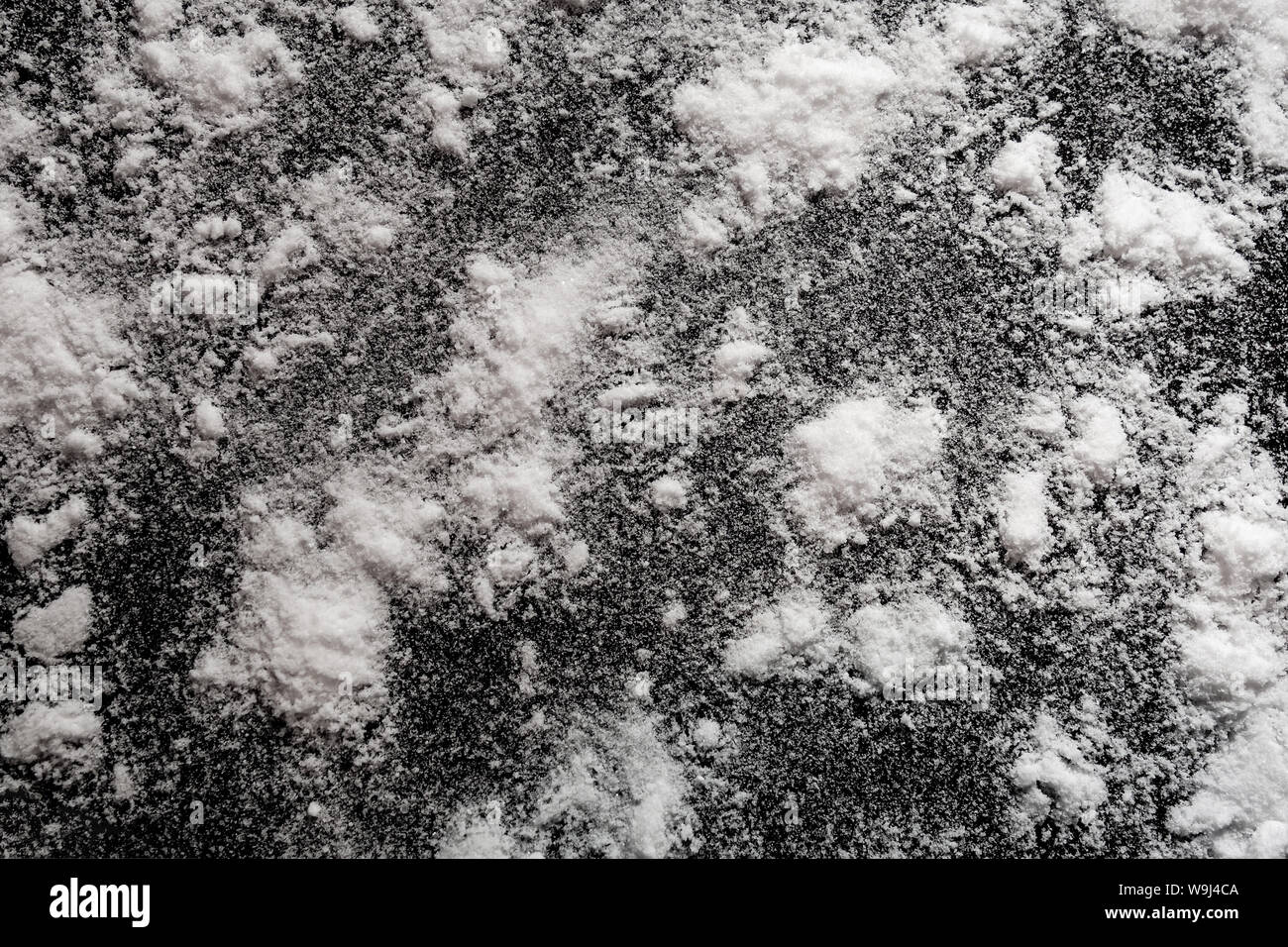 Polvere bianca su sfondo nero. Isolati modello astratto per la cottura, medico o chimico decorazione design. Close up di cristalli pila con random Foto Stock