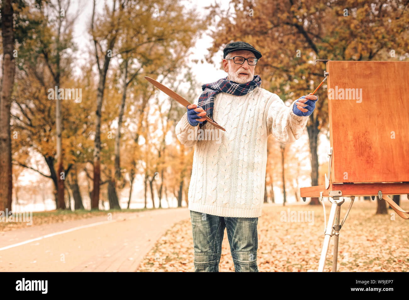 Bello il senior uomo pittura nel parco autunnali Foto Stock