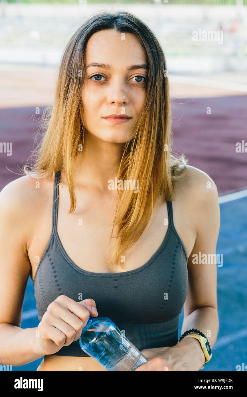 Giovane donna europea con una bottiglia di acqua dopo il jogging all'aperto in Lisabone. Indossa un coperchio grigio e una luce gambali dello sport Foto Stock