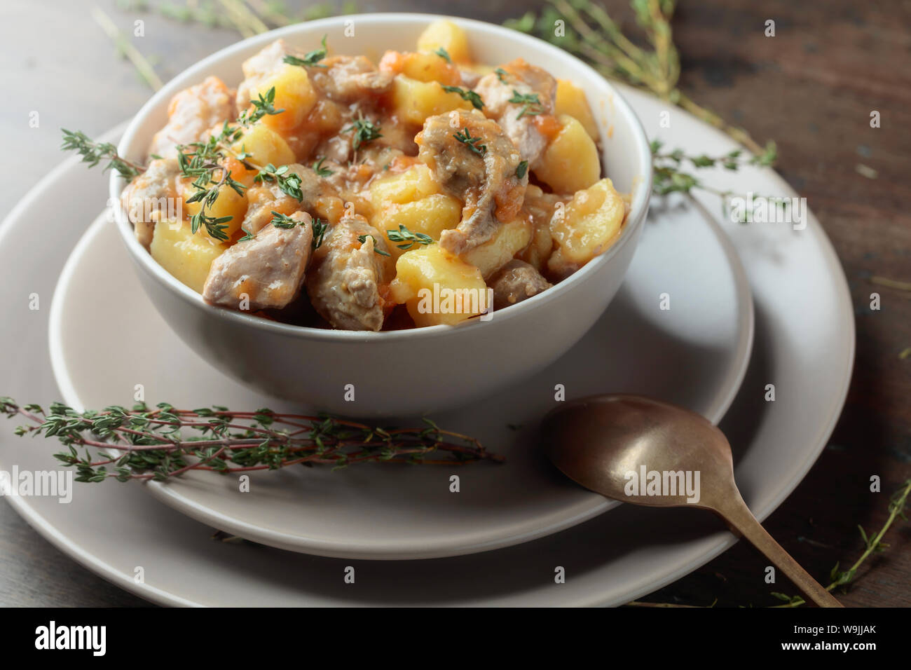 Stufato irlandese cosparso con timo verde. La carne in umido con patate, carote e spezie su sfondo di legno. Foto Stock