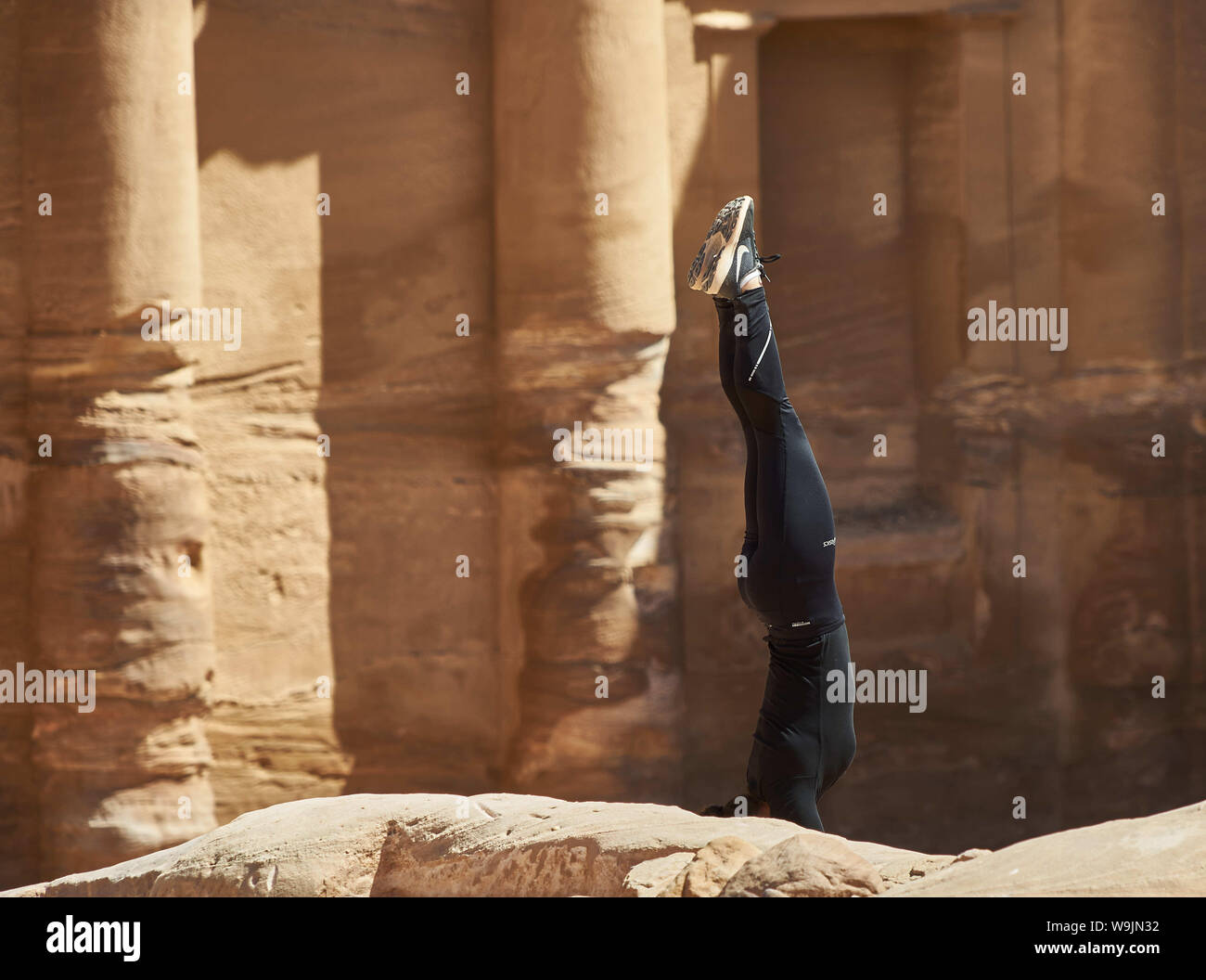 Petra, Giordania, 9 marzo, 2018: giovane ragazza in un nero tuta sportiva è la formazione di un handstand di fronte all'antico monastero Al-Deir. Nel momento in cui sorge Foto Stock